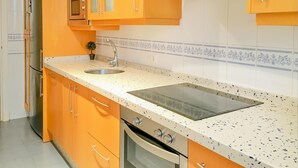 Une cuisine avec des meubles de couleur orange, un plan de travail blanc à motifs, un évier en acier inoxydable et un four encastré.