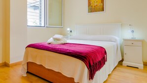 Quarto com cama, mesa de cabeceira, janela e um quadro na parede.