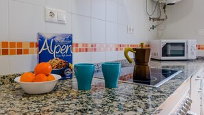 Cozinha com micro-ondas, cafeteira, uma embalagem de cereal Alpen e uma tigela de laranjas sobre bancada de granito.