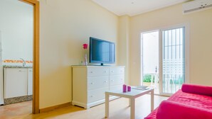 Uma sala de estar moderna com uma TV de tela plana sobre um móvel branco, uma mesinha branca e um sofá rosa vibrante.