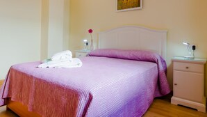 A neatly made bed with a pink and purple striped bedspread, a white headboard, and a nightstand with a lamp and a vase with a single flower. - Ribera E 13489 in El Puerto de Santa Mar a (El Puerto de Santa Maria)