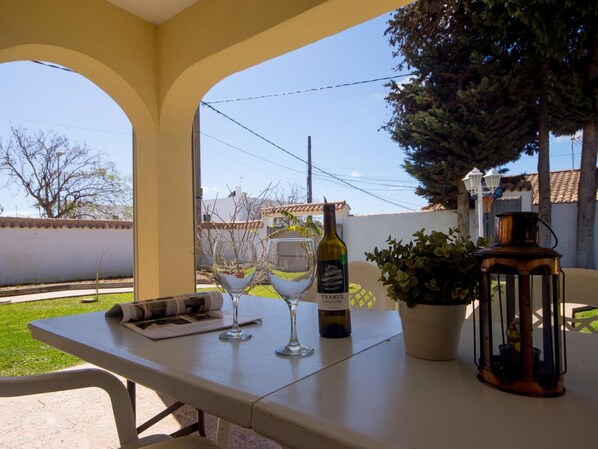 Un patio al aire libre con una mesa dispuesta para dos personas, que incluye una botella de vino, dos copas de vino, un farol y una planta en maceta.