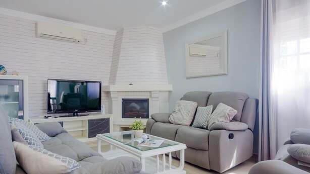 Una sala de estar moderna con chimenea, sofás grises, una mesa de centro de vidrio y un televisor de pantalla plana.