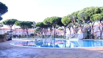 A swimming pool with a curved edge, surrounded by trees and buildings with red roofs.