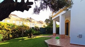 A residential property with a well-maintained lawn, a patio area with steps leading to a covered entrance, and a view of neighboring houses. - Villa Mar De Las Redes 25903 (El Puerto de Santa Maria)