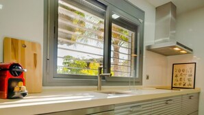 A modern kitchen with a large window, stainless steel appliances, and a wooden cutting board.