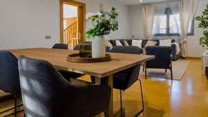 A modern living room with a wooden dining table, black chairs, a sofa, and a large window with curtains.