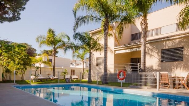 A swimming pool with a clear blue water surface, surrounded by palm trees and a building with a balcony.