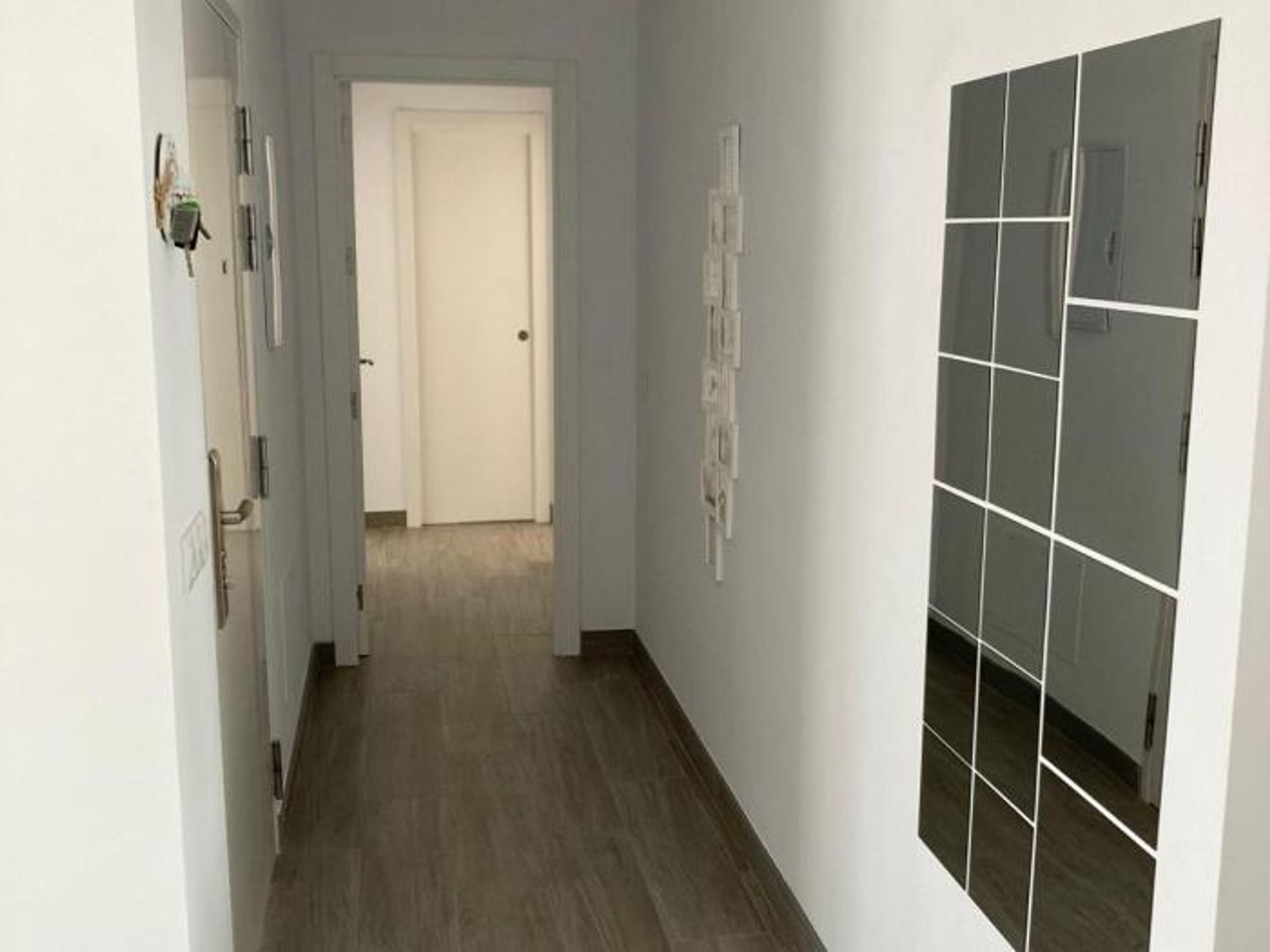 Ein Flur mit Holzboden, einer weißen Tür am Ende und einer Wand mit einem gitterartigen Muster.