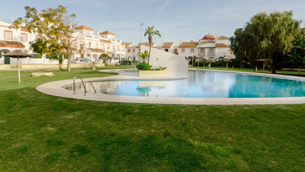 A swimming pool surrounded by a well-maintained lawn, with buildings in the background. - Apartaclub 14116 in Chiclana (Chiclana de la Frontera)