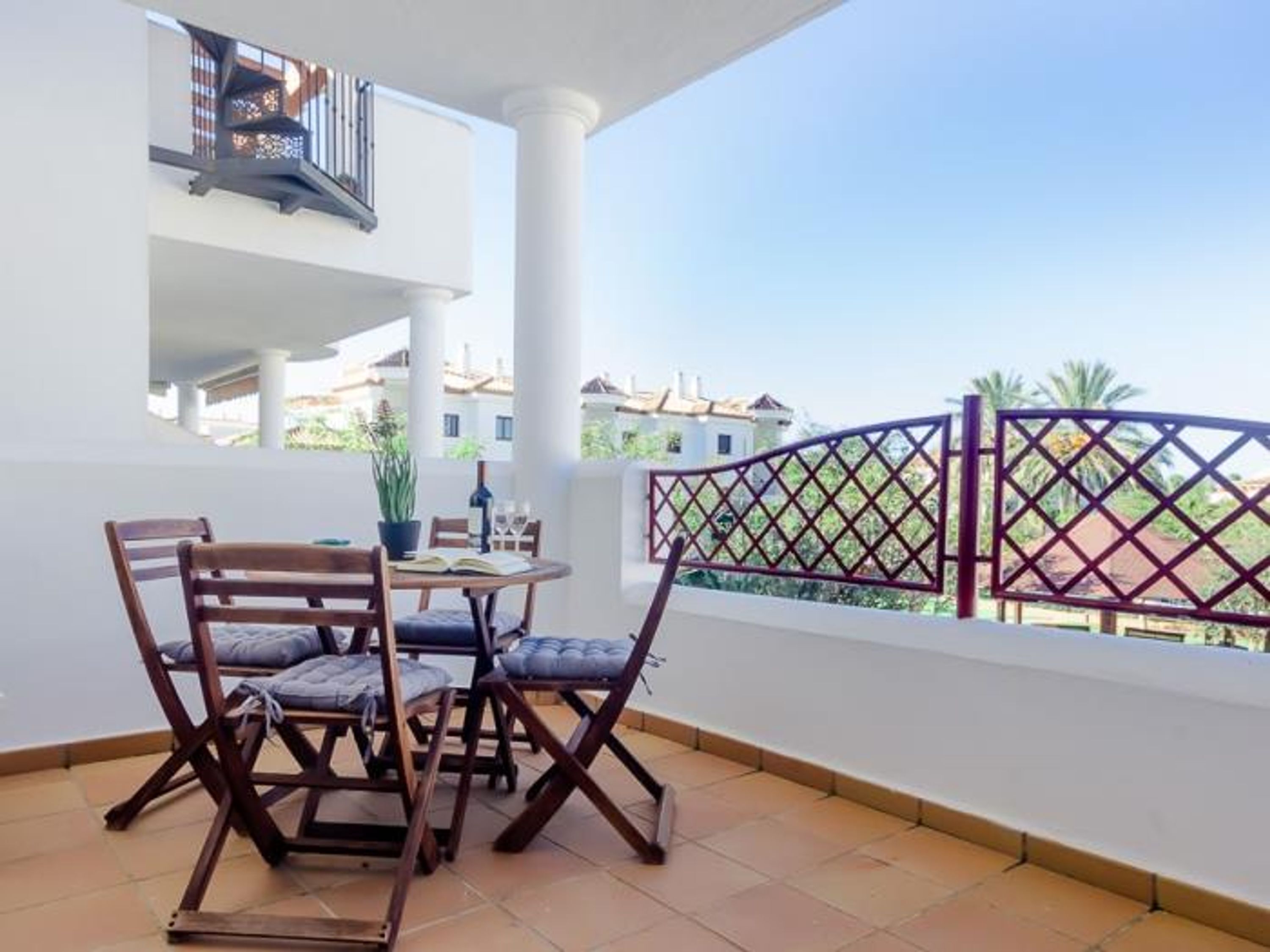 A balcony with a table and chairs, a potted plant, and a view of neighboring buildings.