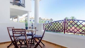 A balcony with a table and chairs, a potted plant, and a view of neighboring buildings.