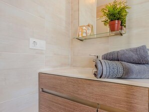 Une salle de bain avec un meuble-lavabo en bois, une étagère en verre ornée d’une plante et une serviette.