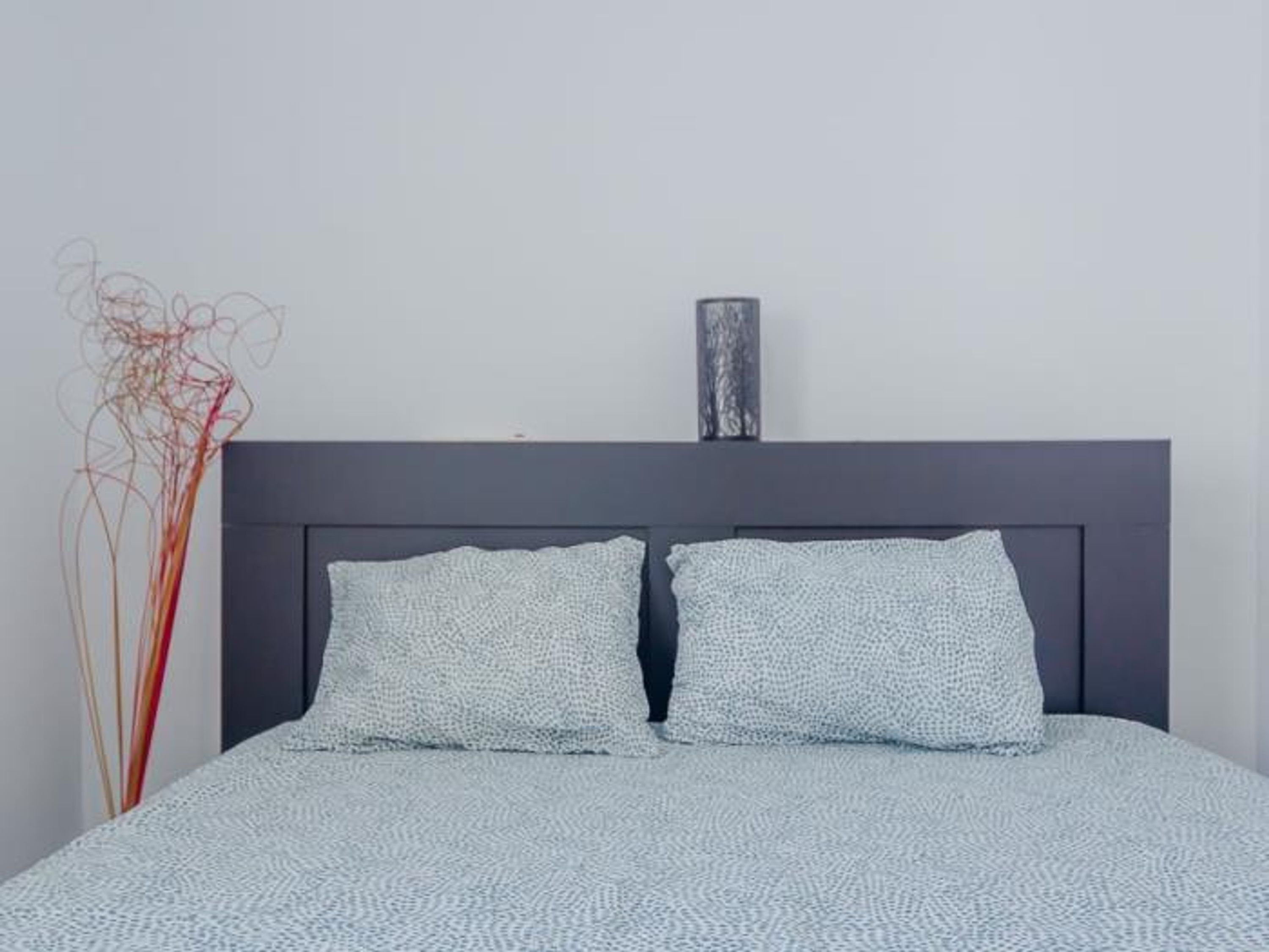 A bed with a grey headboard, two pillows, and a vase on the wall.