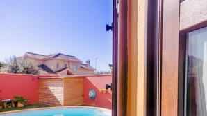 A pool area with a wooden deck, a red wall, and a house in the background. - Villa Las Palomas 14988 (Chiclana de la Frontera)