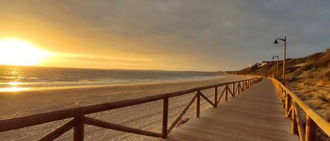 A wooden boardwalk leading to a beach with a sunset in the background.