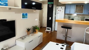 A modern living room with a flat-screen TV, white furniture, a small plant, and a painting. - Ancora P3E 18669 (El Puerto de Santa Maria)