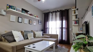 A living room with a sofa, a coffee table, and a ceiling fan. There are bookshelves with books and framed pictures on the walls. - Ancora P3E 18669 (El Puerto de Santa Maria)