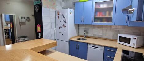 Una cocina compacta con armarios azules, un refrigerador blanco, un microondas y un lavavajillas.