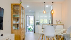 Une cuisine moderne avec des meubles blancs, un coin repas avec des chaises blanches et un meuble en bois contenant de la verrerie.