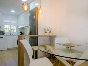 Una cocina moderna con armarios blancos, un refrigerador de acero inoxidable y una mesa de comedor de vidrio con sillas.