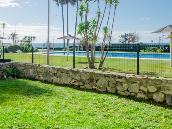 A stone wall, a grassy area, and a pool with a fence.