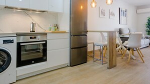 Une cuisine moderne équipée d’appareils électroménagers en acier inoxydable, d’un four encastré et d’un lave-linge. Un coin repas avec une table et des chaises est également disponible.
