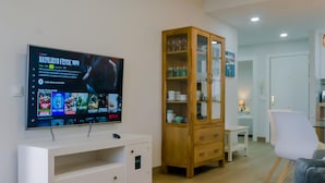 Un salon avec un téléviseur à écran plat fixé sur un meuble TV blanc, un buffet en bois avec des portes en verre et un canapé gris.