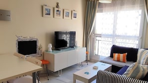 A modern living room with a TV, sofa, dining table, and chairs. There are framed pictures on the wall and a window with curtains. - Ancora P3D 24259 (El Puerto de Santa Maria)
