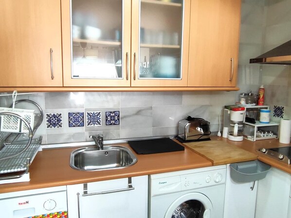 Una cocina con armarios de madera, un lavamanos de acero inoxidable, un tostador, una cafetera y una lavadora.