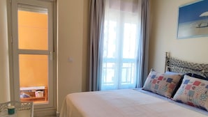 A bedroom with a bed, a chair, a window with curtains, and a painting on the wall. - Ancora P3D 24259 (El Puerto de Santa Maria)