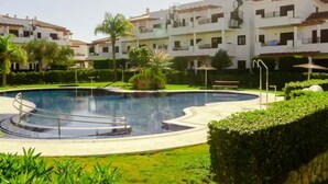 A swimming pool with a circular design, surrounded by well-maintained greenery and a row of white buildings with balconies.