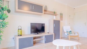 A modern living room with a flat-screen TV, grey cabinets, a white table, and a wooden chair.