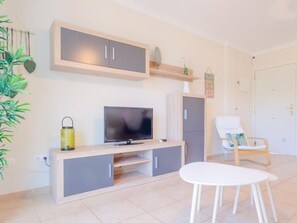 Una sala de estar moderna con un televisor de pantalla plana, armarios grises, una mesa blanca y una silla de madera.