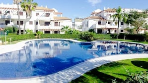 A swimming pool surrounded by white buildings with red-tiled roofs, palm trees, and well-maintained greenery. - Coto de Sancti Petri 9 (Chiclana de la Frontera)