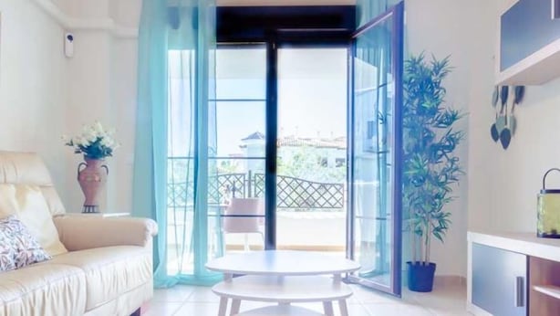 A modern living room with a sofa, a small round table, and a view of a balcony with outdoor furniture. - Coto de Sancti Petri 9 (Chiclana de la Frontera)