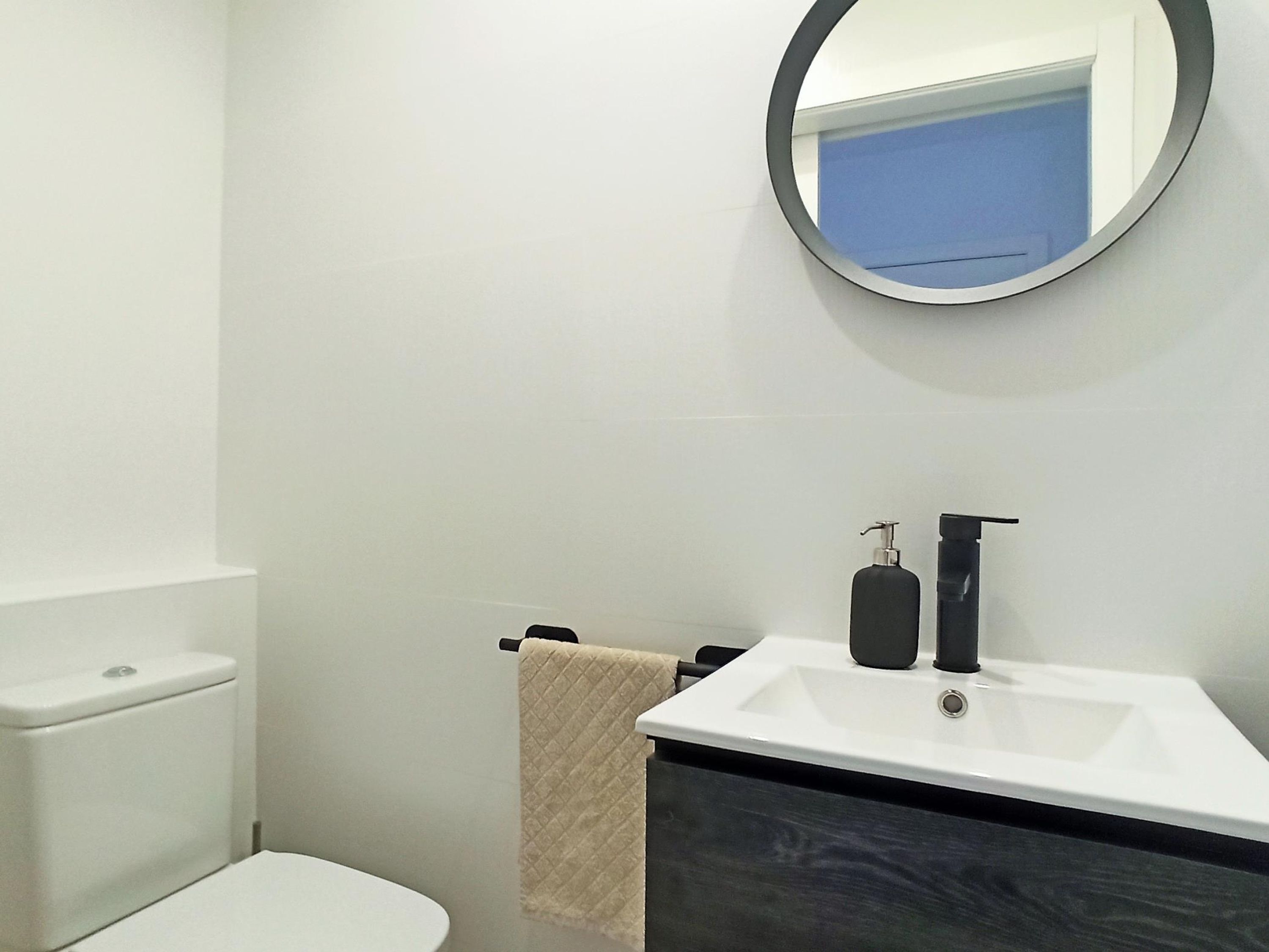 Une salle de bain moderne avec des toilettes blanches, un lavabo doté d’un plan-vasque foncé et un miroir au-dessus du lavabo.