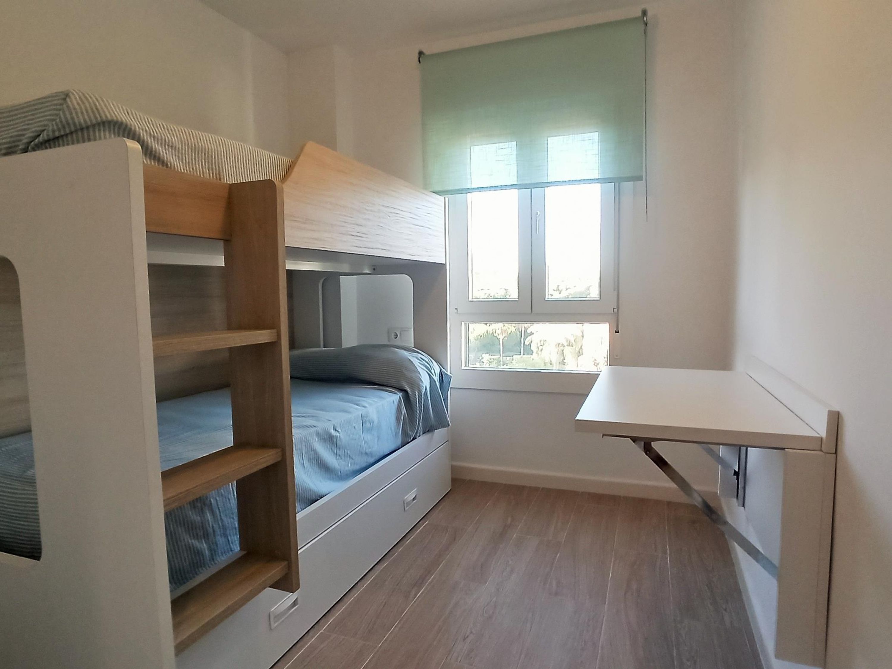 A compact room with a bunk bed, a desk, and a window.