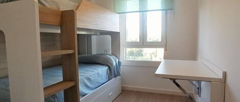 A compact room with a bunk bed, a desk, and a window.