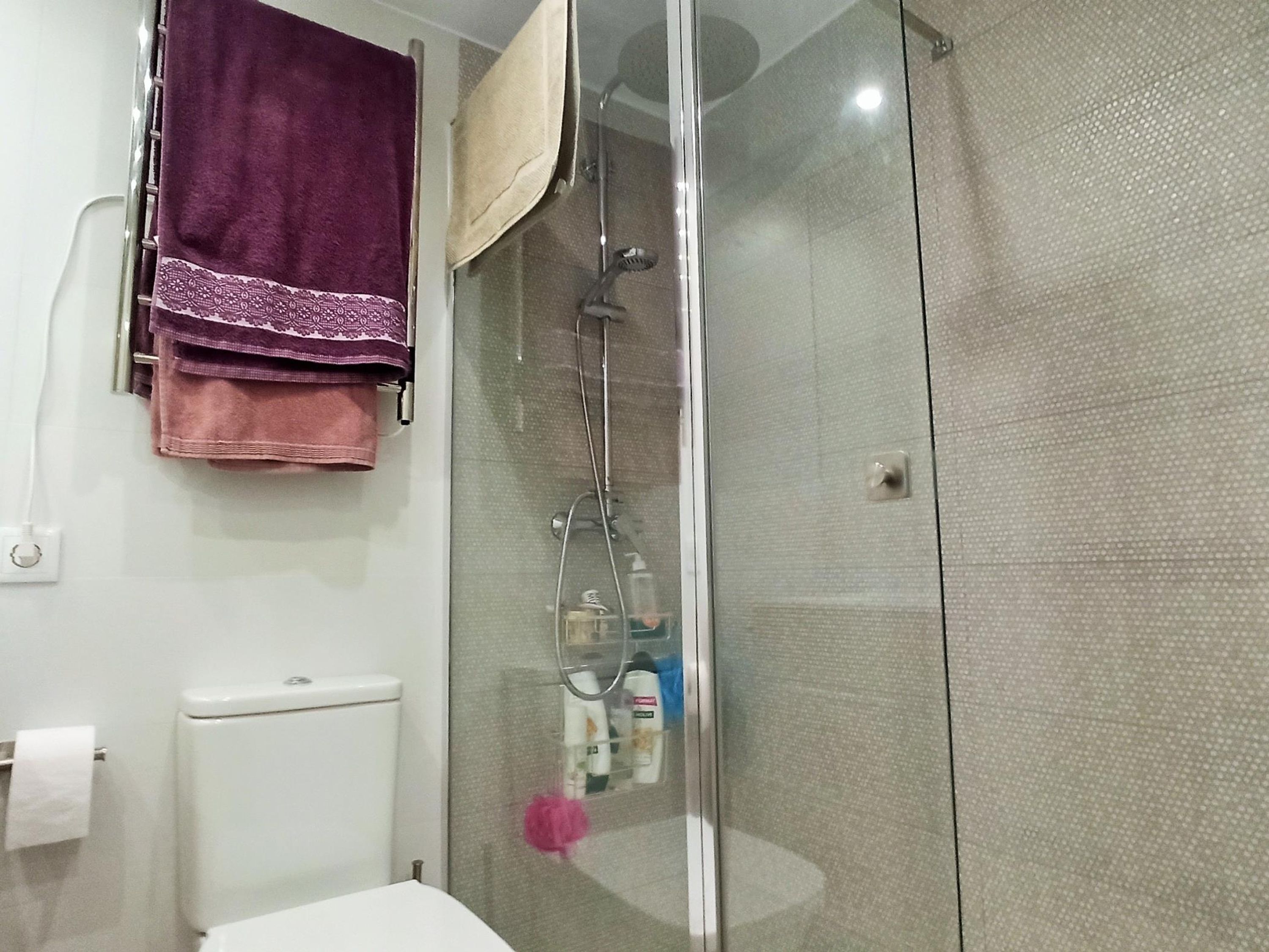 Un baño con cabina de ducha de vidrio, inodoro y perchero con varias toallas.