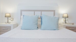 A neatly made bed with two pillows, a bedside table with a lamp, and a wall-mounted painting above the bed. - La Giralda 16584 in Chiclana (Chiclana de la Frontera)