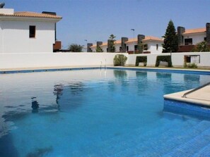 A swimming pool with a clear blue water surface, surrounded by white buildings with red-tiled roofs.
