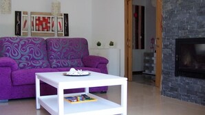 A modern living room with a purple sofa, a white coffee table with books, and a stone fireplace. - Dunas 13 in Chiclana (Chiclana de la Frontera)