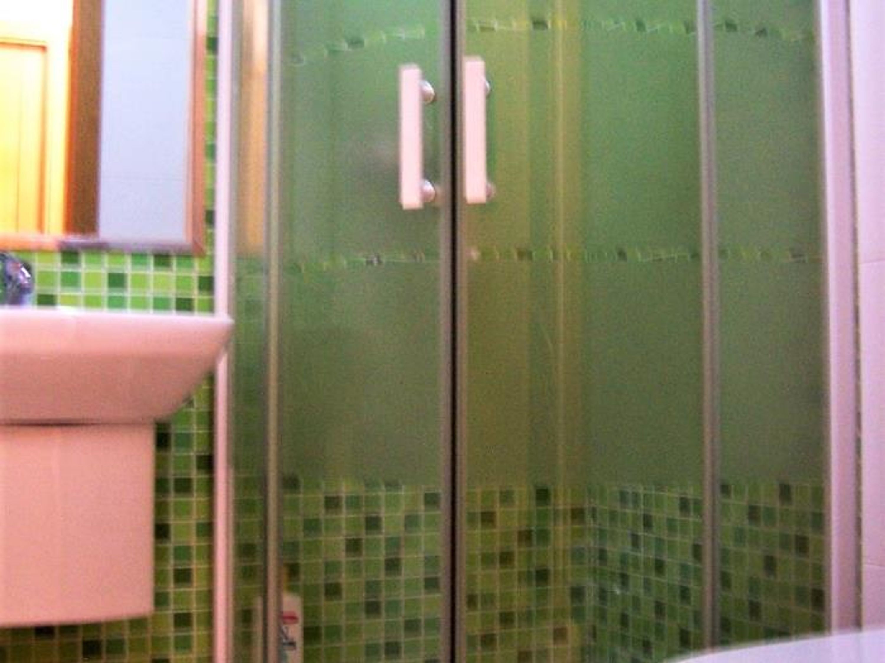A bathroom with a green tiled floor, a white sink, and a glass shower enclosure.