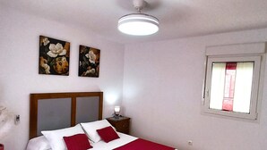 Una camera da letto con un letto, un comodino, una ventola a soffitto e due quadri floreali appesi al muro.