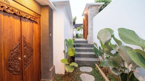 A wooden door with intricate carvings, a stone staircase, and lush green plants. - Daruma Villa Sebatu (Sebatu)