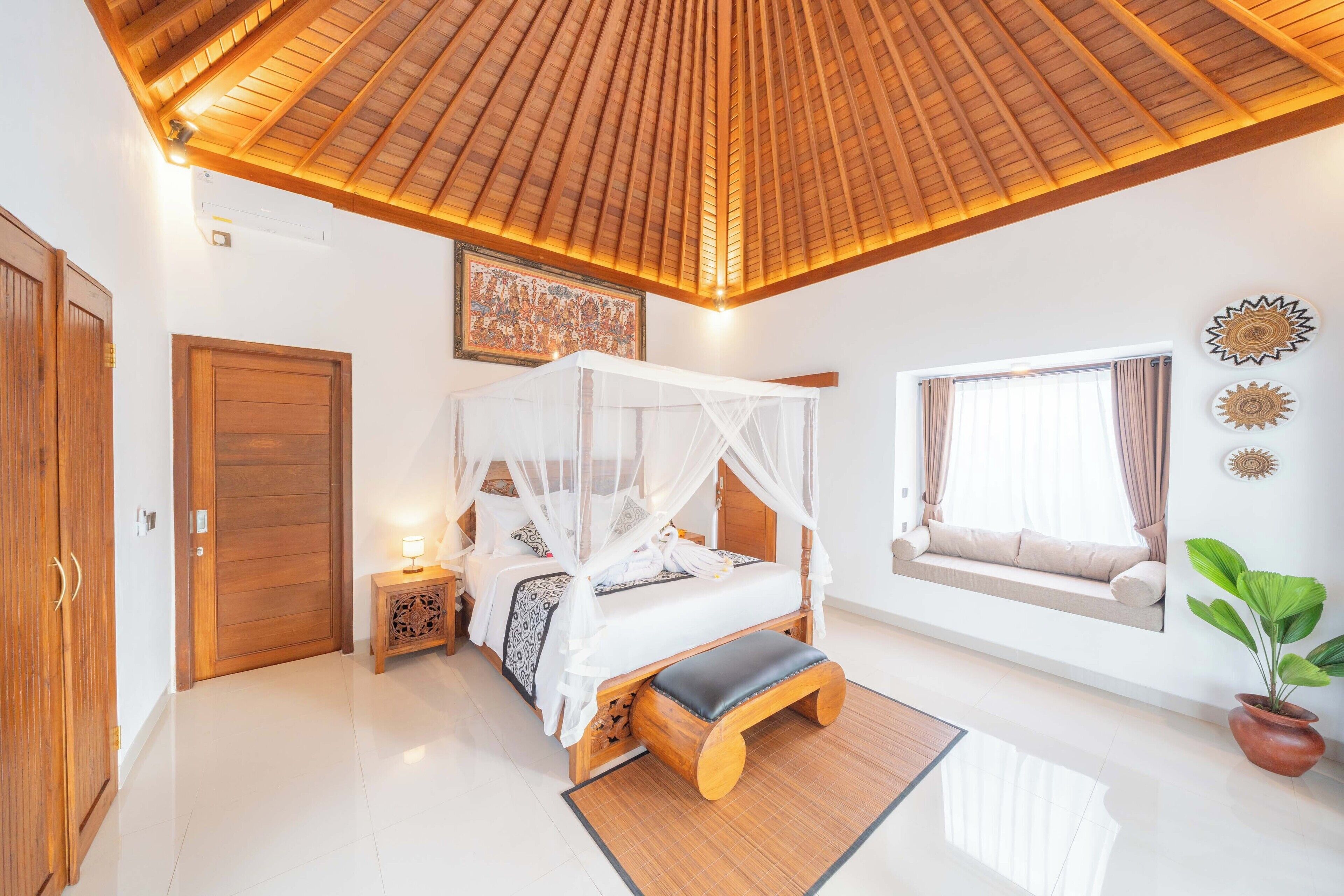 A bedroom with a wooden ceiling, a bed with a canopy, a bedside table with a lamp, a window with a view, and a potted plant.
