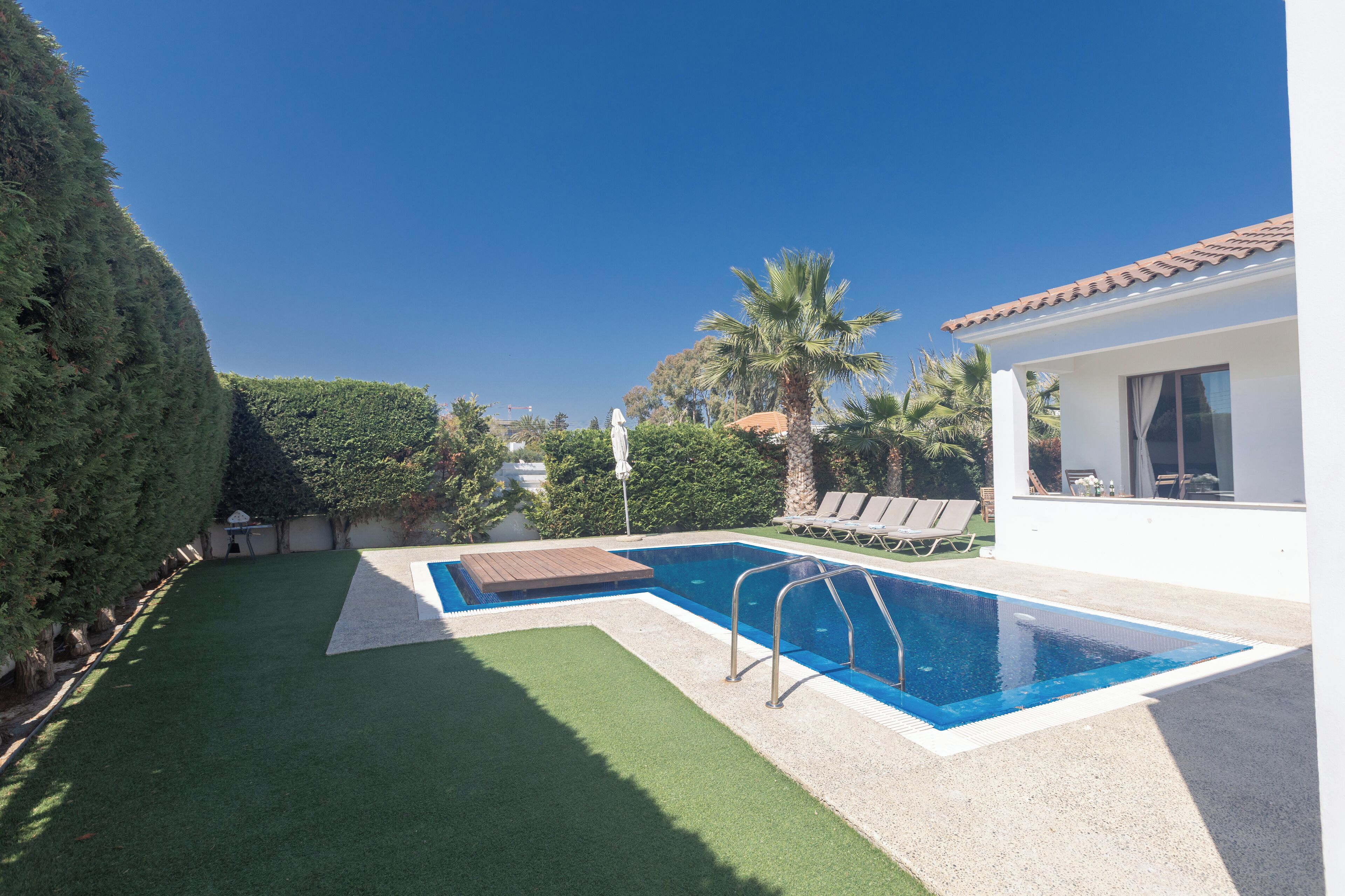 A swimming pool with a wooden deck, surrounded by a well-maintained lawn and palm trees.