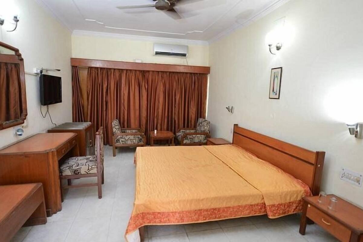 Een hotelkamer met een bed, een bureau, een stoel, een televisie en een plafondventilator.