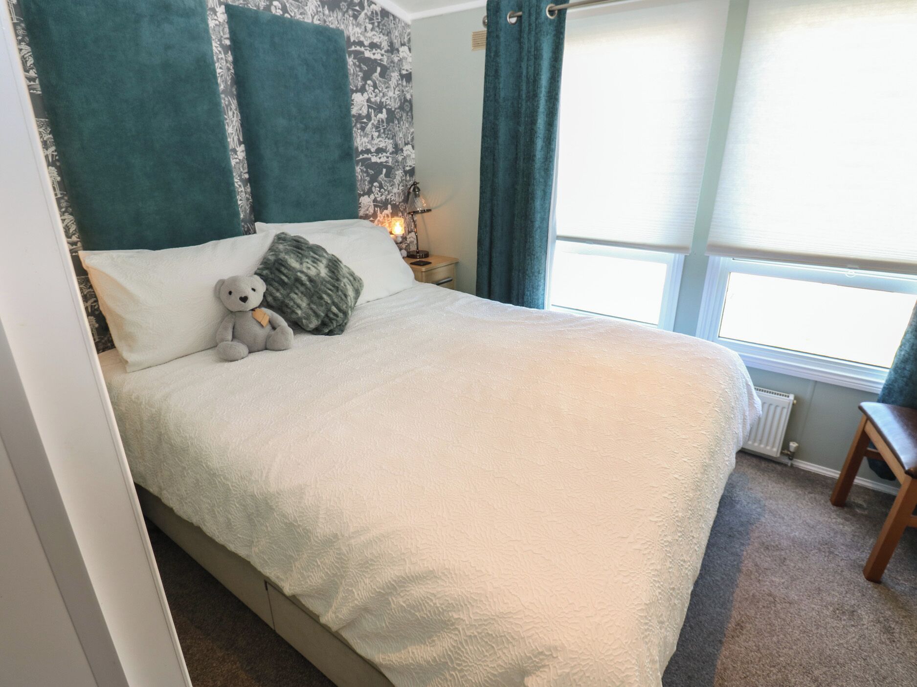 Un lit bien fait, recouvert d’une couverture blanche moelleuse, avec un ours en peluche et un oreiller à texture particulière.